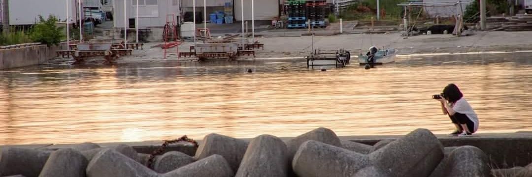 夕焼けの海辺でカメラを構えるフルサワアスカ